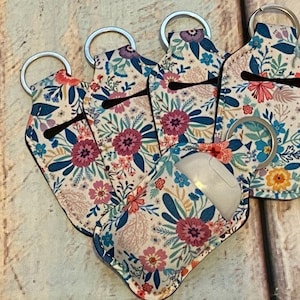 May include: Five floral patterned hand sanitizer holders with key rings. The holders are made of a soft, flexible material and have a zippered closure. The holders are all different colors and patterns.