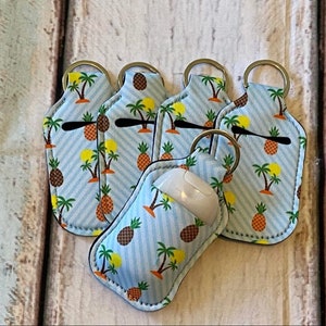 May include: A collection of keychains with a tropical pineapple and palm tree pattern on a light blue striped background. One keychain holds a white wireless mouse. Each keychain has a metal ring.