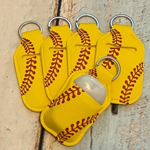 May include: Six yellow and red softball-themed hand sanitizer holders with silver keychains. The holders are made of fabric and have a clear plastic window for the sanitizer bottle.