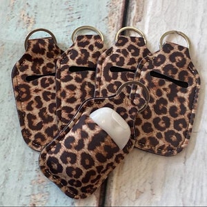 May include: Five leopard print hand sanitizer holders with keychains. The holders are made of a soft, flexible material and have a small opening for a hand sanitizer bottle.