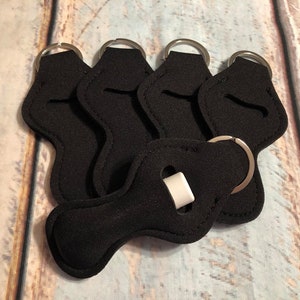 May include: Six black lip balm holders with silver key rings. The holders are made of a soft, flexible material and have a small opening for the lip balm to be inserted.