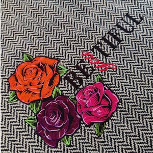 Könnte beinhalten: Ein schwarzer und weißer Chevron-Stoff mit dem Text "Beautiful" in schwarzer Stickerei. Drei gestickte Rosen in Rot, Pink und Lila sind in Herzform angeordnet.
