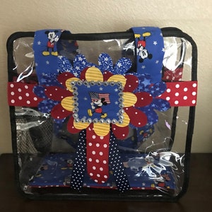 May include: Clear plastic tote bag with a red, white, and blue Mickey Mouse design. The bag has a black mesh pocket on the front and a red and white polka dot ribbon.