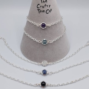 May include: Four silver chain bracelets with different coloured gemstones. The gemstones are set in a hexagonal shape. The bracelets are displayed on a grey cone with the text "The Crafty Tom Cat" written on it.