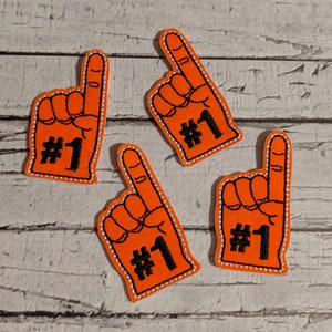 May include: Four orange foam finger cutouts with black stitching and silver glitter. Each finger has the number "#1" written on it.