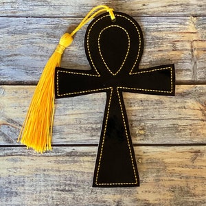 May include: Black leather bookmark shaped like an Ankh, an ancient Egyptian symbol of life. The bookmark has yellow stitching and a yellow tassel.