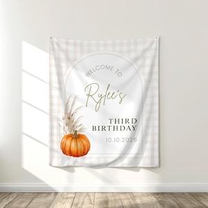 May include: A beige and white checkered banner with the text "Welcome to Rylee's Third Birthday 10.10.2025". The banner features a watercolor illustration of a pumpkin and pampas grass.
