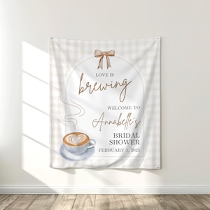Op de afbeelding: Banner met een lichtbeige ruitjespatroon achtergrond. De tekst "Love is brewing" staat boven "Welcome to Annabelle's Bridal Shower February 1, 2025". Een aquarel afbeelding van een koffiekopje met een hartontwerp staat links.