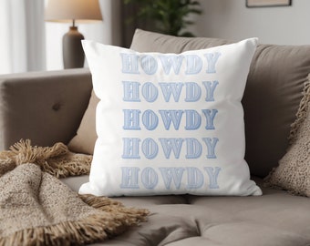 Puede incluir: Almohada blanca con la palabra "HOWDY" repetida cinco veces en azul claro. La palabra está en una fuente estilizada con un doble contorno.