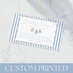 May include: A custom printed baby shower invitation card with a blue and white striped border. The card features the text "Display Shower" and a watercolor illustration of baby clothes hanging on a clothesline. The bottom of the card reads "CUSTOM PRINTED".