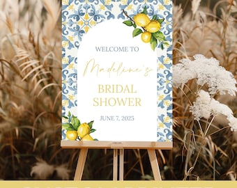 May include: A custom printed bridal shower sign on a wooden easel. The sign features a blue and yellow tile pattern with an arch shape. Text reads "Welcome to Madeline's Bridal Shower June 7, 2025". Lemon illustrations are on the sign.