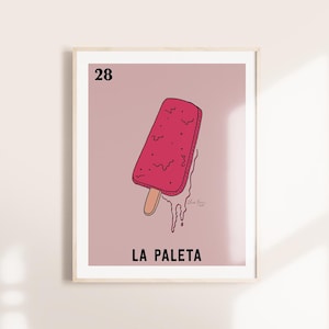 May include: A framed print featuring a red popsicle on a stick, with the number 28 at the top and the words "LA PALETA" at the bottom. The popsicle is melting, with drips of red liquid. The background is a light pink.