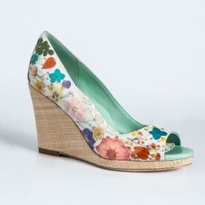K&ouml;nnte beinhalten: Ein Paar hellgr&uuml;ne Keilschuhe mit Blumenmuster. Die Schuhe haben eine offene Zehenpartie und einen geflochtenen Keilabsatz.
