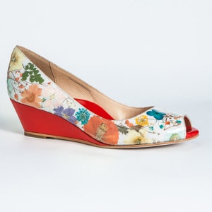 May include: A white peep-toe wedge shoe with a floral print and a red wedge heel.