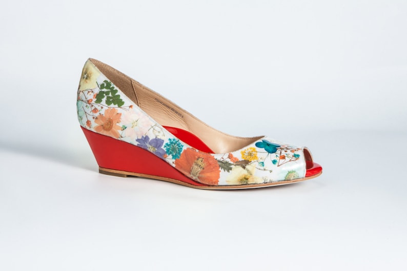 May include: A white peep-toe wedge shoe with a floral print and a red wedge heel.