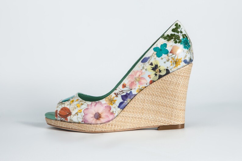 K&ouml;nnte beinhalten: Ein wei&szlig;er Keilabsatz mit Blumenmuster und einem nat&uuml;rlichen gewebten Keil. Der Schuh hat eine offene Zehenpartie und ein gr&uuml;nes Futter.