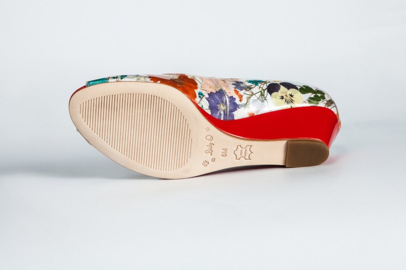 May include: The bottom of a floral print wedge heel shoe with a red sole. The shoe is a size 8 and is made of leather.
