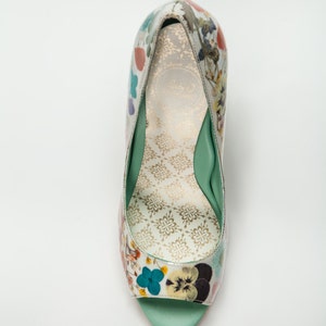 K&ouml;nnte beinhalten: Ein einzelner gr&uuml;ner und wei&szlig;er Damenschuh mit floralem Muster, Peeptoe und Absatz und gr&uuml;ner Innensohle.