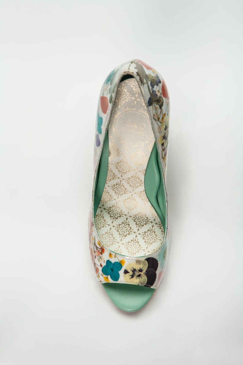 K&ouml;nnte beinhalten: Ein einzelner gr&uuml;ner und wei&szlig;er Damenschuh mit floralem Muster, Peeptoe und Absatz und gr&uuml;ner Innensohle.