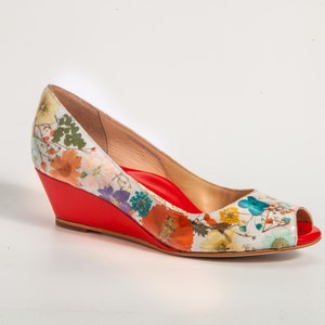 May include: A white wedge shoe with a red platform and a floral print. The shoe has a peep toe and a pointed toe.