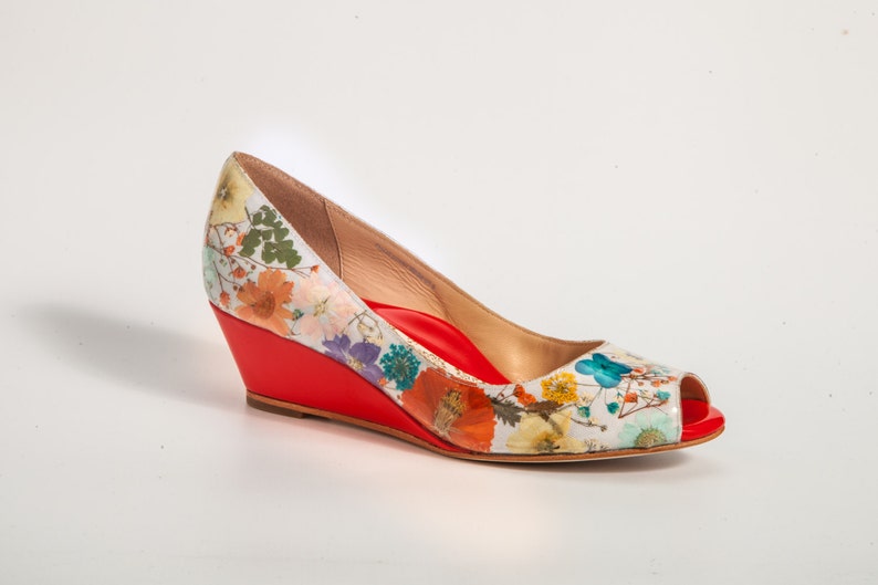 May include: A white wedge shoe with a red platform and a floral print. The shoe has a peep toe and a pointed toe.