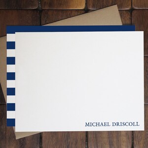 May include: A white card with blue and white stripes on the left side. The card has a blue border at the top and the text "MICHAEL DRISCOLL" at the bottom.