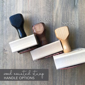 three different types of wood-mounted stamp handles, each with a distinct color and finish, arranged on a wooden surface.