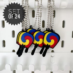 May include: A set of 24 keychains featuring a colorful design with red, yellow, and blue accents. Each keychain has a black stick and a silver ball chain. The keychains are hanging on a white pegboard.