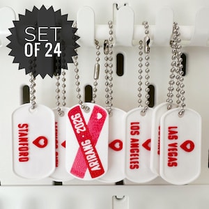 May include: A set of 24 white dog tags with silver ball chains. The tags feature red text and heart graphics, with locations like Stanford, Los Angeles, and Las Vegas. One tag has a pink ribbon design with the text "ARIRANG 2026".