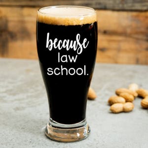 May include: A clear glass beer mug with a black liquid inside. The mug has the text "because law school." printed on the side.