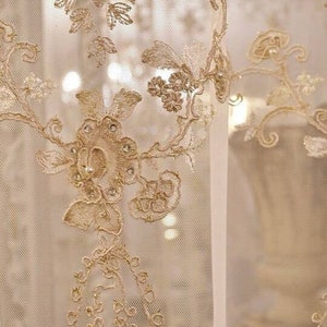 May include: Close-up of a sheer white curtain with delicate gold embroidery. The embroidery features floral patterns and intricate details.