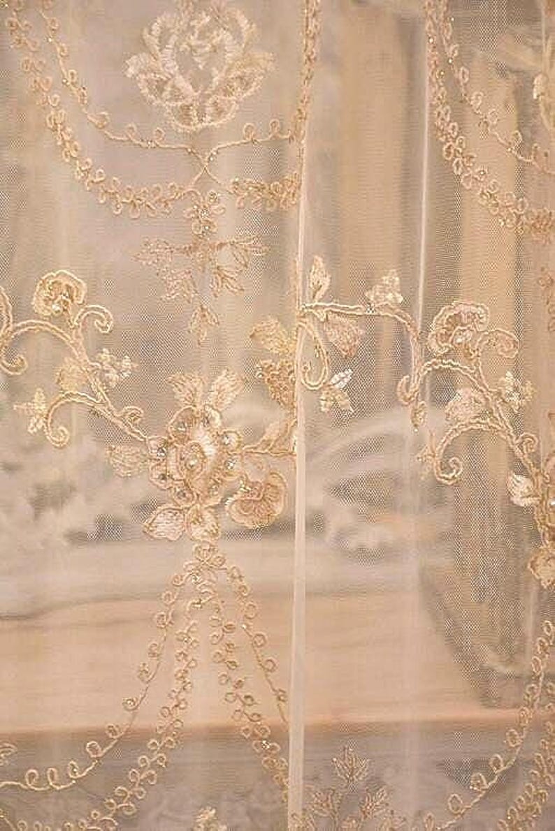 May include: A pair of sheer white curtains with delicate gold embroidery featuring floral patterns. The embroidery is intricate and detailed, creating a luxurious and elegant look.