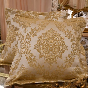 Peut inclure: Deux coussins décoratifs avec un fond blanc et un motif damassé doré. Les coussins sont faits d'un tissu doux et luxueux et ajouteraient une touche d'élégance à n'importe quelle pièce.