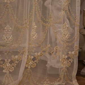 May include: A sheer white curtain with delicate gold embroidery and beaded accents. The curtain has a scalloped bottom edge and a floral pattern.