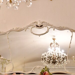 May include: A large, ornate, white, ornately carved mirror with a crystal chandelier reflected in the glass.