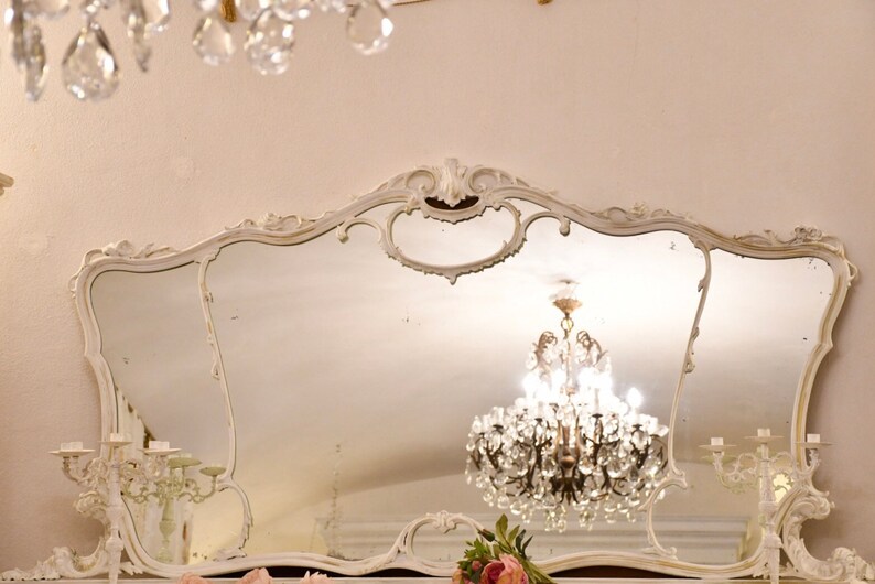 May include: A large, ornate, white, ornately carved mirror with a crystal chandelier reflected in the glass.