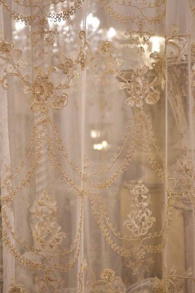 May include: A sheer white curtain with delicate gold embroidery featuring floral and vine patterns. The embroidery is intricate and adds a touch of elegance to the curtain.