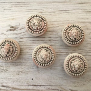 Pode incluir: Cinco botões de cerâmica branca com um design de cabeça de leão em relevo. Cada botão tem uma borda decorativa.