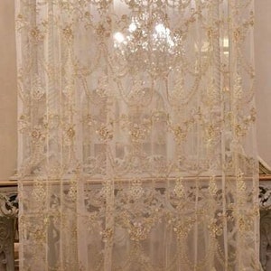 May include: White sheer curtains with a delicate floral pattern and gold embroidery. The curtains are hung in a room with a large window and a chandelier.