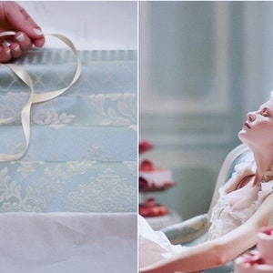 May include: A woman in a white dress and a large white hat with feathers is reclining in a blue and white chair. A pink cake with red berries is on a table in the background.