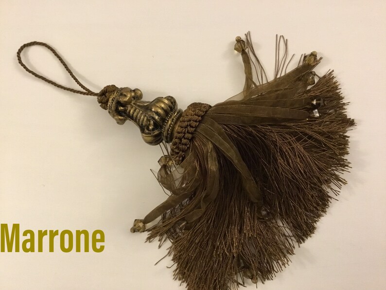 May include: A brown tassel with a gold-colored metal top. The tassel is made of a soft, fluffy material and has a long, thin cord.