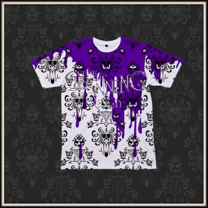 May include: A white t-shirt with a purple and black Haunted Mansion pattern. The pattern features the iconic wallpaper design with dripping purple paint.
