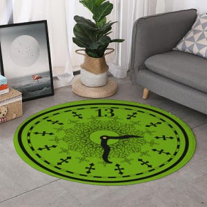 May include: A round, green rug with a clock face design. The rug features a black border, the number "13", and black clock hands. The clock face has a decorative, symmetrical pattern in black. The rug is on a gray floor.