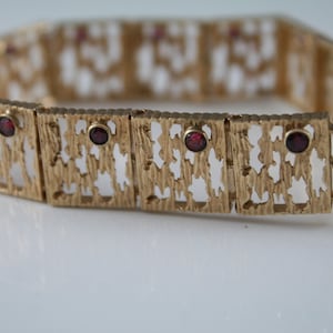 May include: Gold bracelet with a textured design and red gemstones.