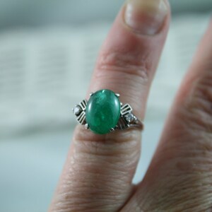 May include: A silver ring with a large oval emerald green gemstone and two smaller diamond accents.