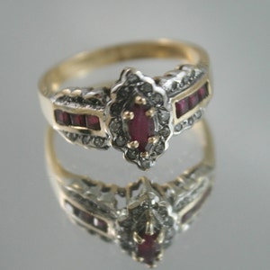 Puede incluir: Un anillo de oro con un rubí rojo y detalles de diamantes. El anillo tiene un diseño delicado con un centro puntiagudo y una banda de rubíes rojos.