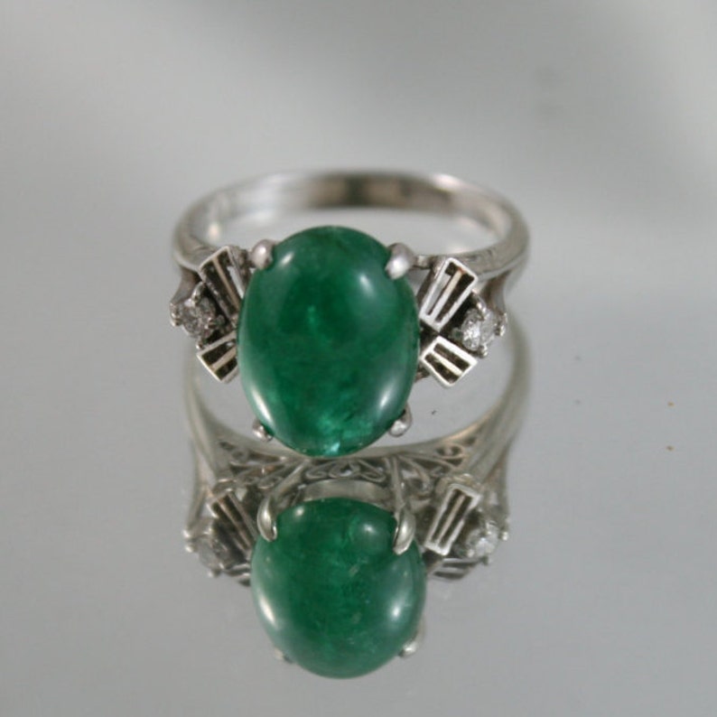 May include: A silver ring with a large, oval-shaped emerald gemstone and smaller diamond accents.