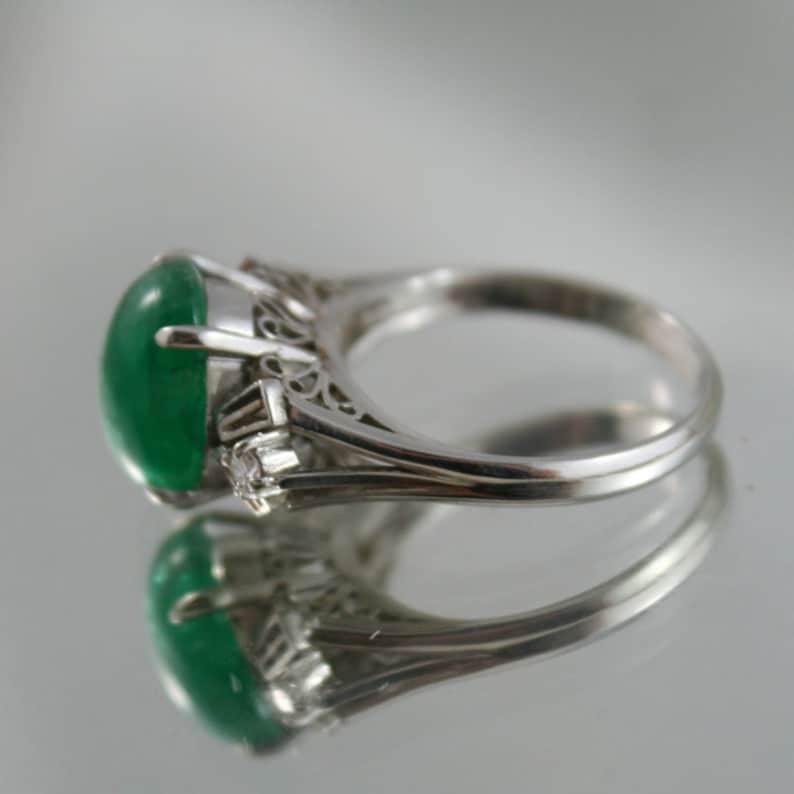 May include: A silver ring with a large, oval-shaped green gemstone and smaller diamond accents. The ring has a delicate, filigree design.