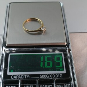 May include: A gold ring with a diamond-shaped stone is displayed on a digital scale. The scale shows a weight of 1.69, with a capacity of 500g x 0.01g. The ring is centered on the scale's silver surface.