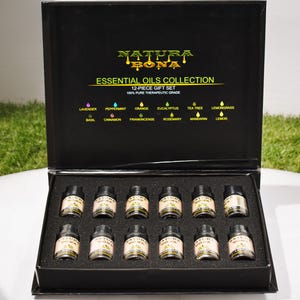 May include: A black rectangular gift box containing 12 small glass bottles of essential oils. The lid interior features the text NATURA BONA ESSENTIAL OILS COLLECTION 12-PIECE GIFT SET 100% PURE THERAPEUTIC GRADE and lists the 12 oil scents.